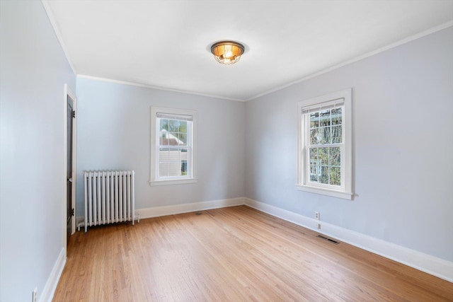 spare room featuring radiator heating unit, plenty of natural light, crown molding, light wood finished floors, and baseboards