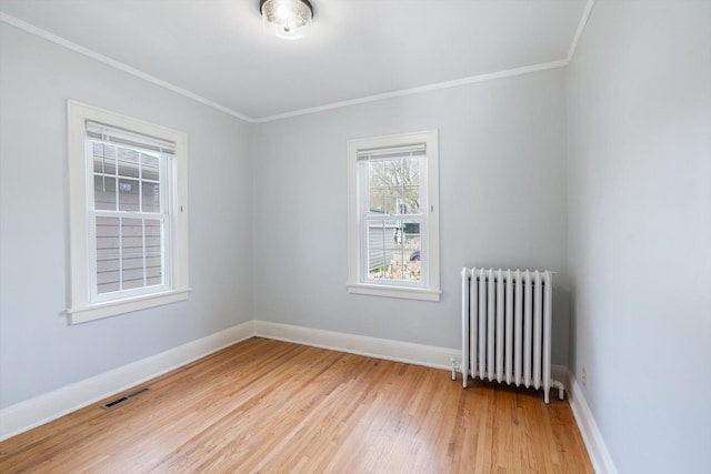empty room featuring radiator heating unit, light wood-style floors, crown molding, and baseboards