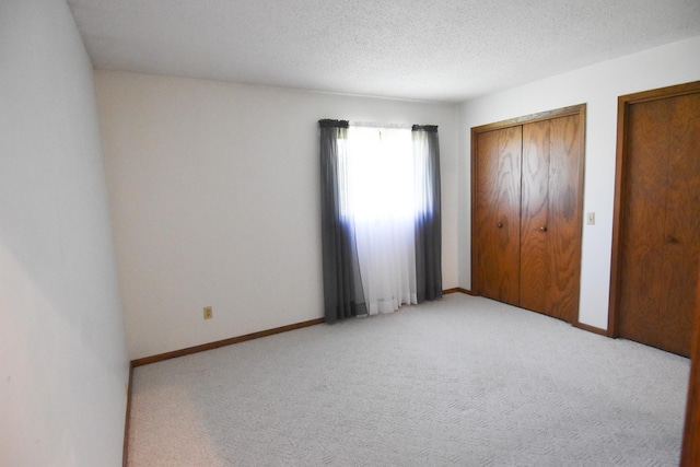 13946 151st St NE, Thief River Falls, MN 56701 - unfurnished bedroom featuring light carpet, multiple closets, baseboards, and a textured ceiling