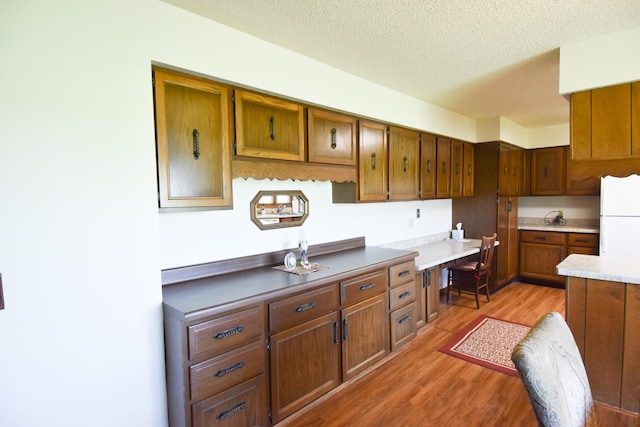 13946 151st St NE, Thief River Falls, MN 56701 - kitchen with freestanding refrigerator, light wood-style floors, brown cabinets, a textured ceiling, and built in desk