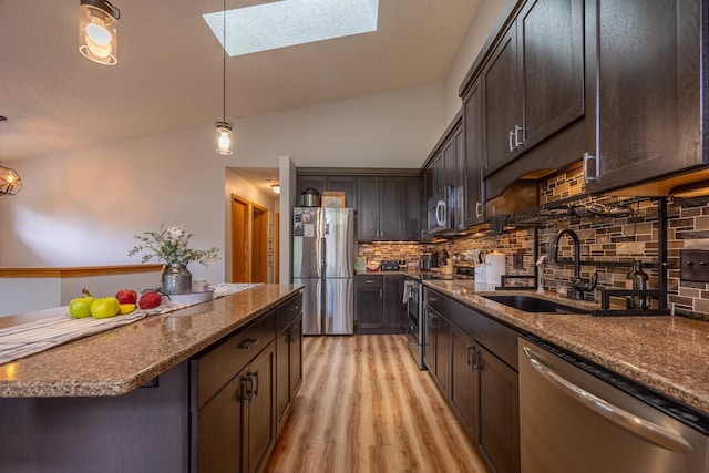 kitchen with stainless steel appliances, a sink, light wood-style floors, a skylight, and tasteful backsplash