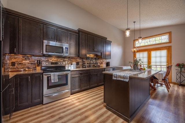 kitchen featuring appliances with stainless steel finishes, light wood-type flooring, dark brown cabinetry, backsplash, and a textured ceiling