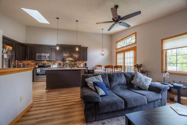living room featuring light wood-style floors, plenty of natural light, a skylight, ceiling fan, and a textured ceiling