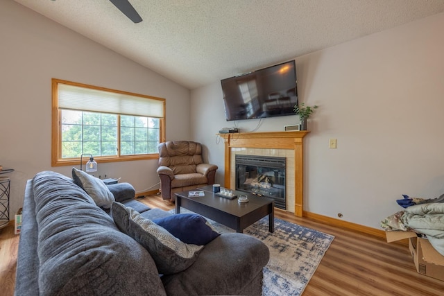 living room with a fireplace, lofted ceiling, wood finished floors, a textured ceiling, and a ceiling fan