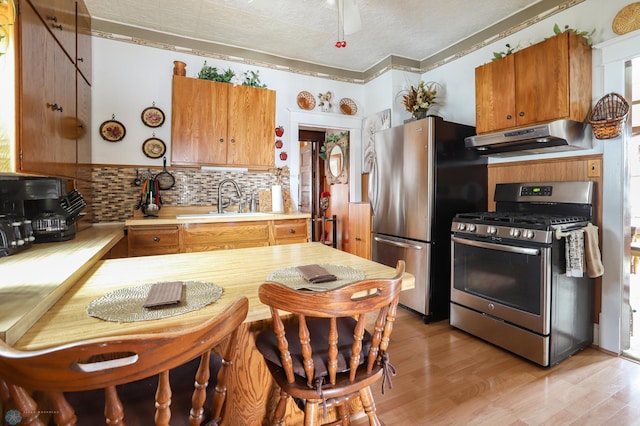 kitchen featuring appliances with stainless steel finishes, under cabinet range hood, a sink, light countertops, and decorative backsplash