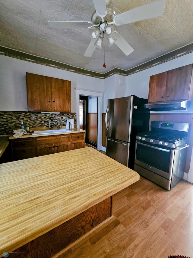 kitchen with appliances with stainless steel finishes, light countertops, under cabinet range hood, ceiling fan, and backsplash