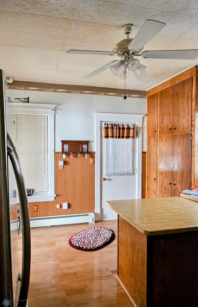 kitchen featuring a baseboard heating unit, wood finished floors, ceiling fan, a wainscoted wall, and wood walls