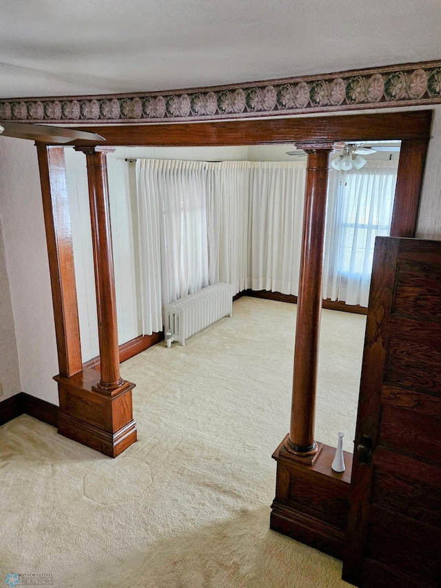 carpeted empty room with radiator heating unit, ornate columns, baseboards, and a ceiling fan