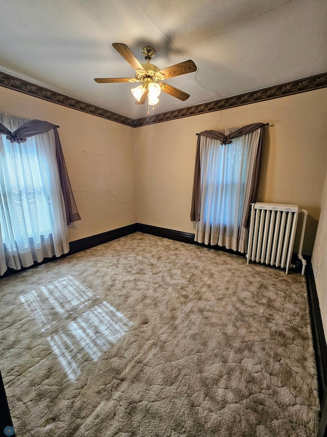 carpeted empty room with radiator, ceiling fan, baseboards, and ornamental molding