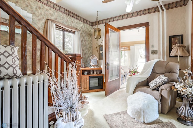 living room featuring radiator, wallpapered walls, carpet, stairway, and ceiling fan