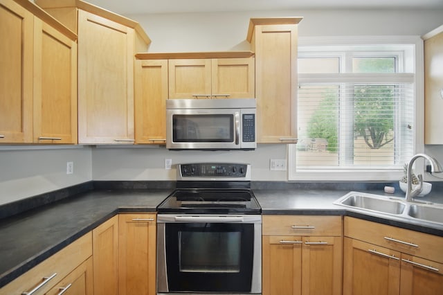 kitchen with appliances with stainless steel finishes, a sink, light brown cabinets, and dark countertops
