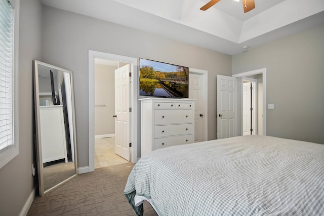 bedroom featuring light colored carpet, ensuite bathroom, baseboards, and a ceiling fan