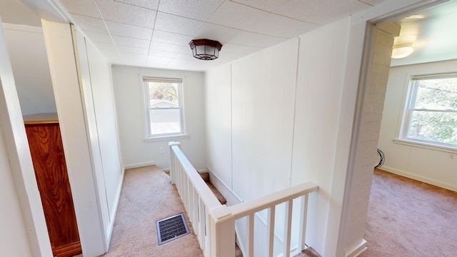 corridor with an upstairs landing, light carpet, healthy amount of natural light, and baseboards