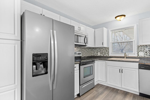 12420 Chippewa Ln, Burnsville, MN 55337 - kitchen with appliances with stainless steel finishes, a sink, dark countertops, white cabinets, and a textured ceiling