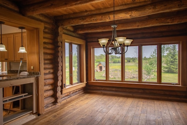 unfurnished sunroom with a chandelier, wood-type flooring, beam ceiling, and rustic walls