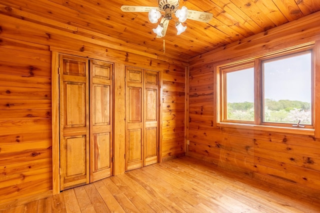 unfurnished bedroom featuring light wood-type flooring, a closet, wooden walls, and a ceiling fan