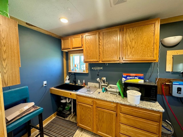 13739 429th Ave, Webster, SD 57274 - kitchen featuring a sink, black microwave, baseboards, light stone countertops, and brown cabinetry
