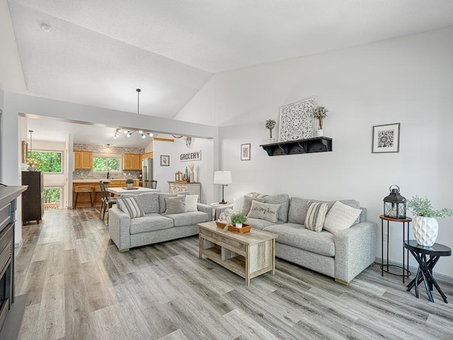living room with lofted ceiling, light wood-style flooring, a glass covered fireplace, and baseboards