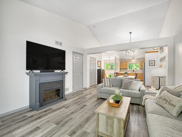 living area with vaulted ceiling, light wood finished floors, a glass covered fireplace, and baseboards