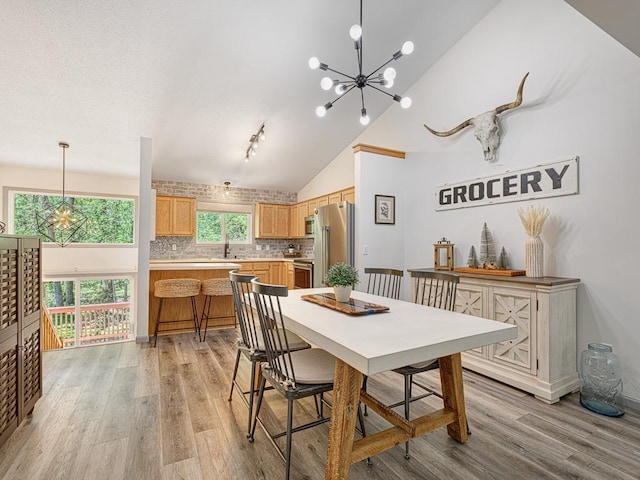 dining area featuring a chandelier, light wood-type flooring, and high vaulted ceiling