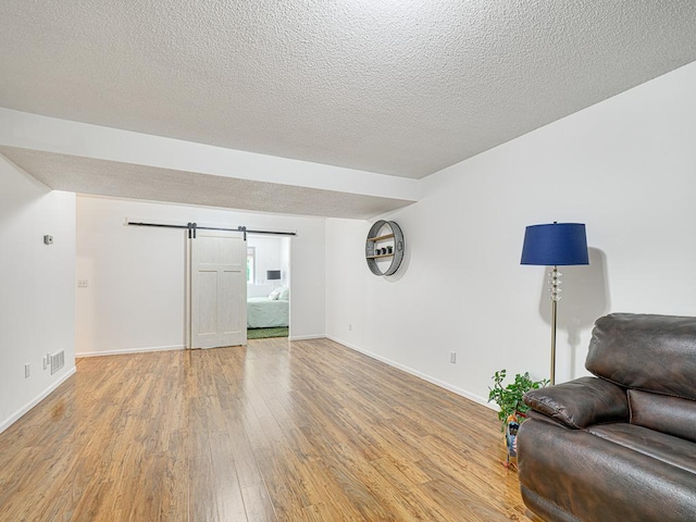 living area featuring a barn door, light wood finished floors, a textured ceiling, and baseboards