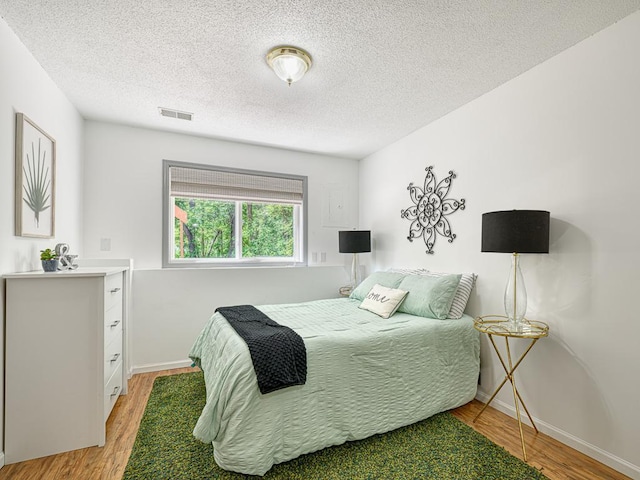 bedroom featuring light wood-type flooring, a textured ceiling, and baseboards