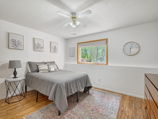 bedroom with wood finished floors, a textured ceiling, baseboards, and a ceiling fan