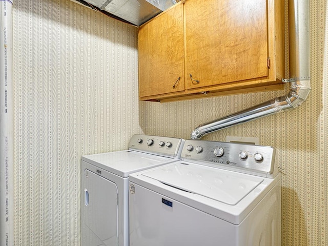 laundry area featuring wallpapered walls, washing machine and dryer, and cabinet space