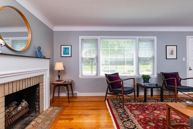 sitting room with light wood finished floors, a brick fireplace, and baseboards