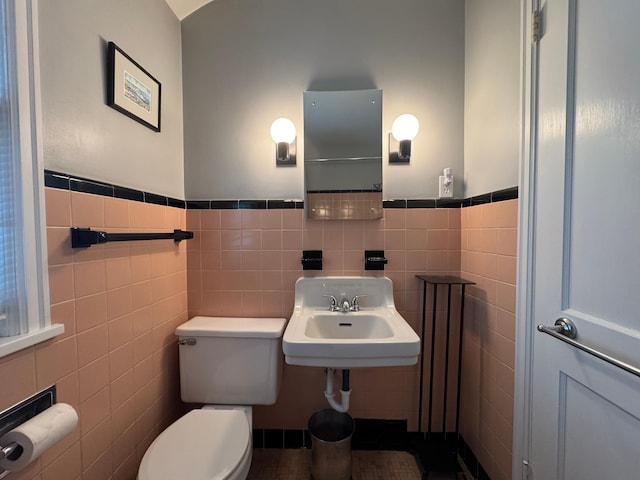 half bath with tile walls, a sink, wainscoting, and toilet