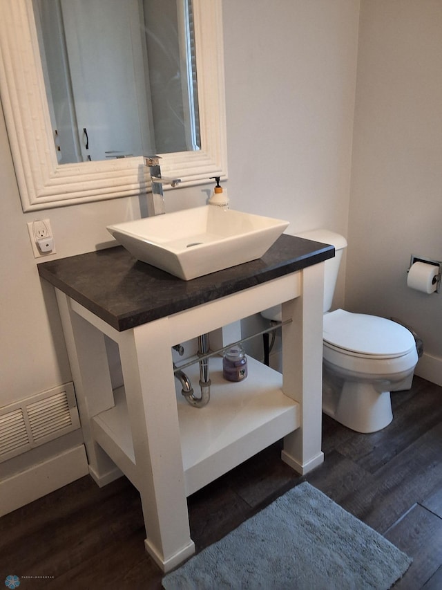half bath featuring wood finished floors, toilet, baseboards, and vanity