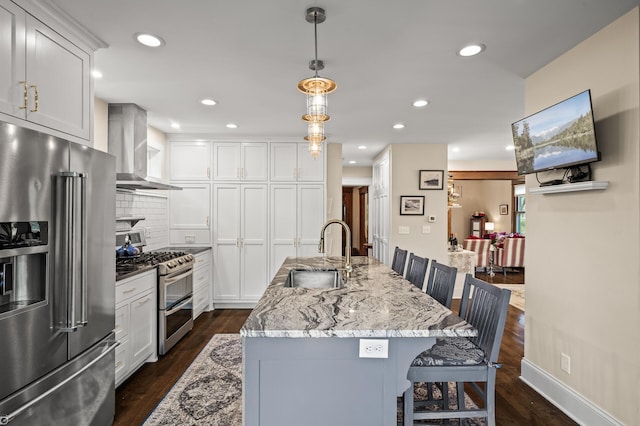 kitchen featuring appliances with stainless steel finishes, a sink, wall chimney exhaust hood, a breakfast bar, and backsplash