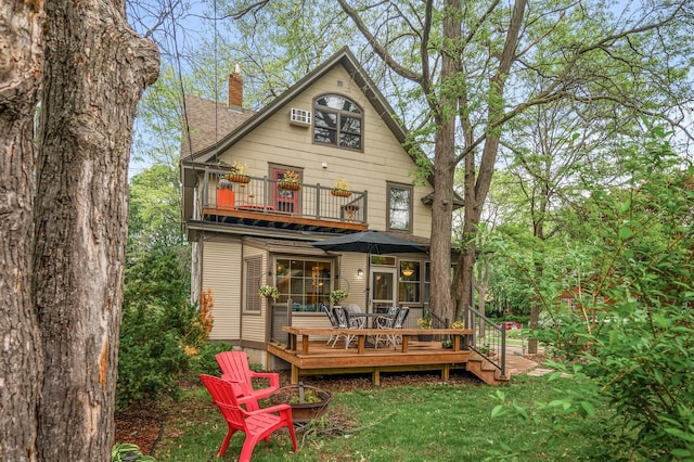 back of house featuring a balcony, a chimney, a yard, a deck, and an outdoor fire pit
