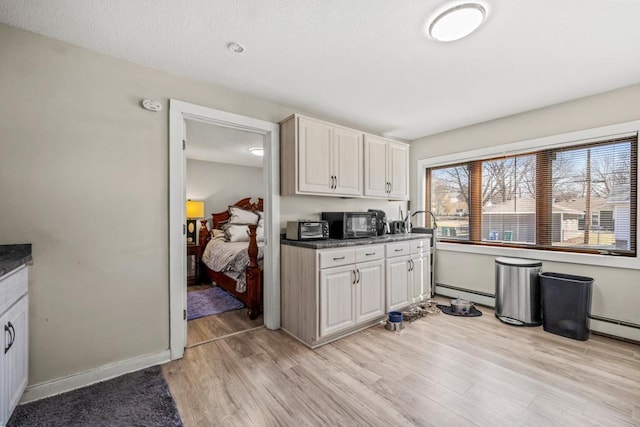 4959 5th St NE, Columbia Heights, MN 55421 - kitchen featuring a baseboard heating unit, light wood-type flooring, white cabinetry, dark countertops, and baseboards