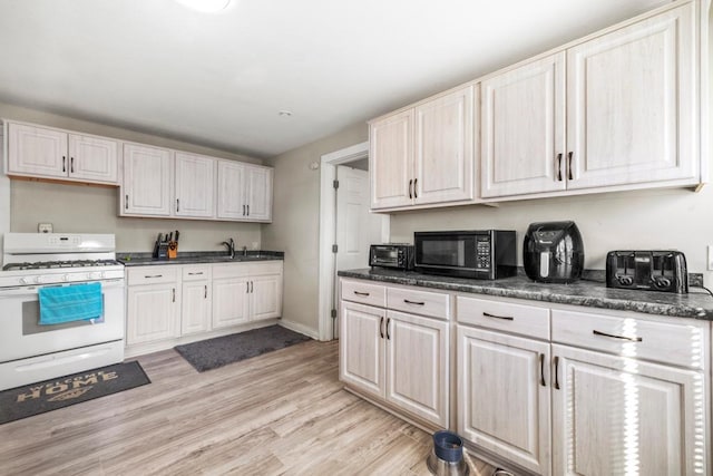 4959 5th St NE, Columbia Heights, MN 55421 - kitchen featuring white range with gas stovetop, black microwave, light wood-style flooring, dark countertops, and a sink