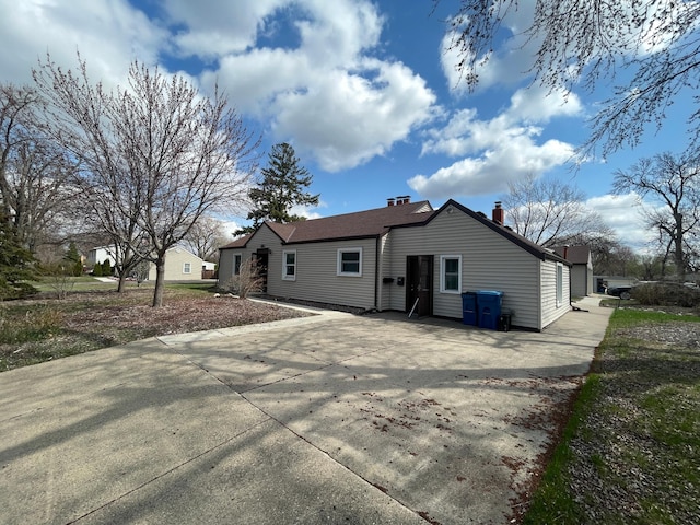 rear view of property featuring a chimney and concrete driveway
