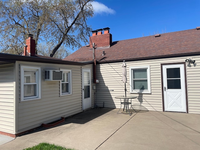 rear view of house featuring a patio, a chimney, a shingled roof, and a wall mounted air conditioner