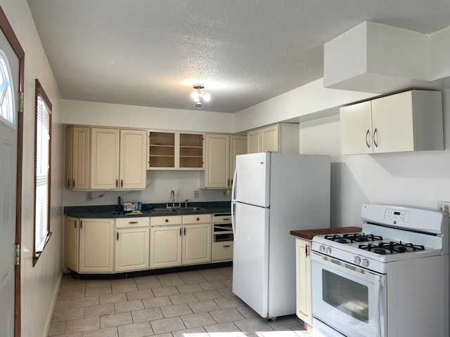 kitchen with white appliances, a sink, cream cabinetry, dark countertops, and open shelves