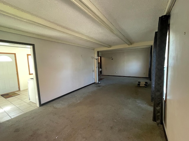 tiled empty room with a textured ceiling, carpet floors, beam ceiling, and baseboards
