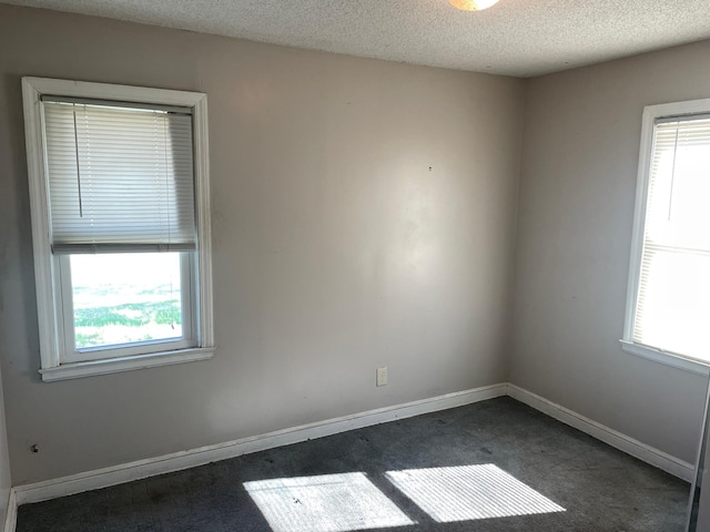 spare room featuring dark carpet, a textured ceiling, and baseboards