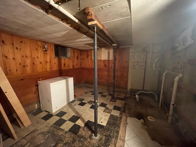 unfinished basement featuring refrigerator, wood walls, and tile patterned floors
