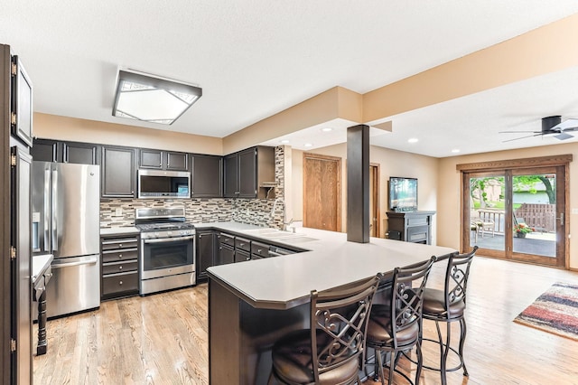 14308 Park Ave, Burnsville, MN 55337 - kitchen featuring stainless steel appliances, light wood-style floors, a peninsula, a kitchen bar, and backsplash