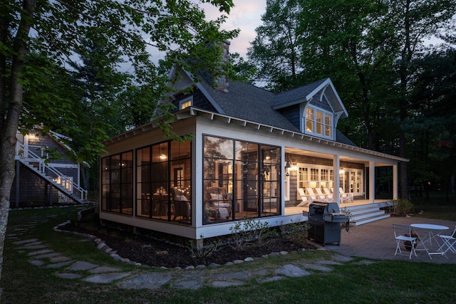 6024 Ojibwa Rd, Brainerd, MN 56401 - back of house at dusk featuring a sunroom, a patio area, and a shingled roof