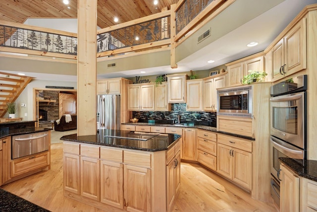 40335 Government Rd, Barry Twp, MN 55037 - kitchen featuring light brown cabinetry, appliances with stainless steel finishes, a warming drawer, a towering ceiling, and a fireplace