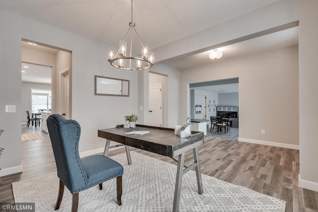 office area with light wood-type flooring, a chandelier, and baseboards