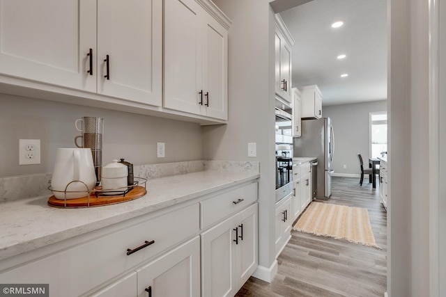 kitchen featuring white cabinets, stainless steel appliances, wood finished floors, light stone counters, and recessed lighting
