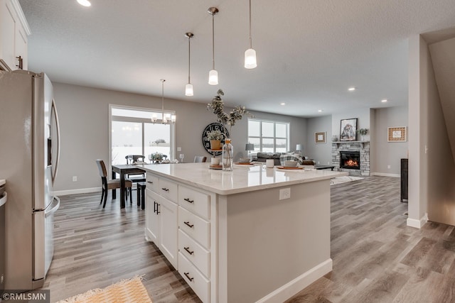 kitchen featuring stainless steel refrigerator with ice dispenser, a stone fireplace, white cabinets, a kitchen island, and recessed lighting