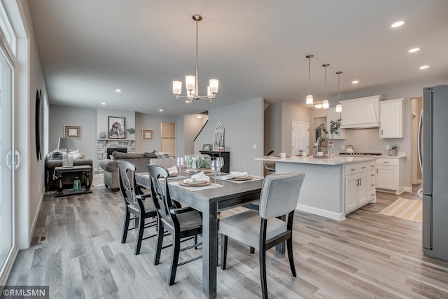 dining space with light wood finished floors, a fireplace, recessed lighting, and a chandelier