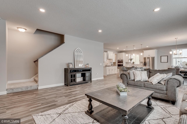 living room featuring light wood finished floors, a chandelier, a textured ceiling, baseboards, and recessed lighting