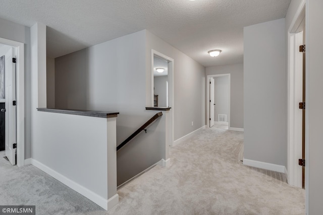 corridor with an upstairs landing, carpet floors, a textured ceiling, and baseboards